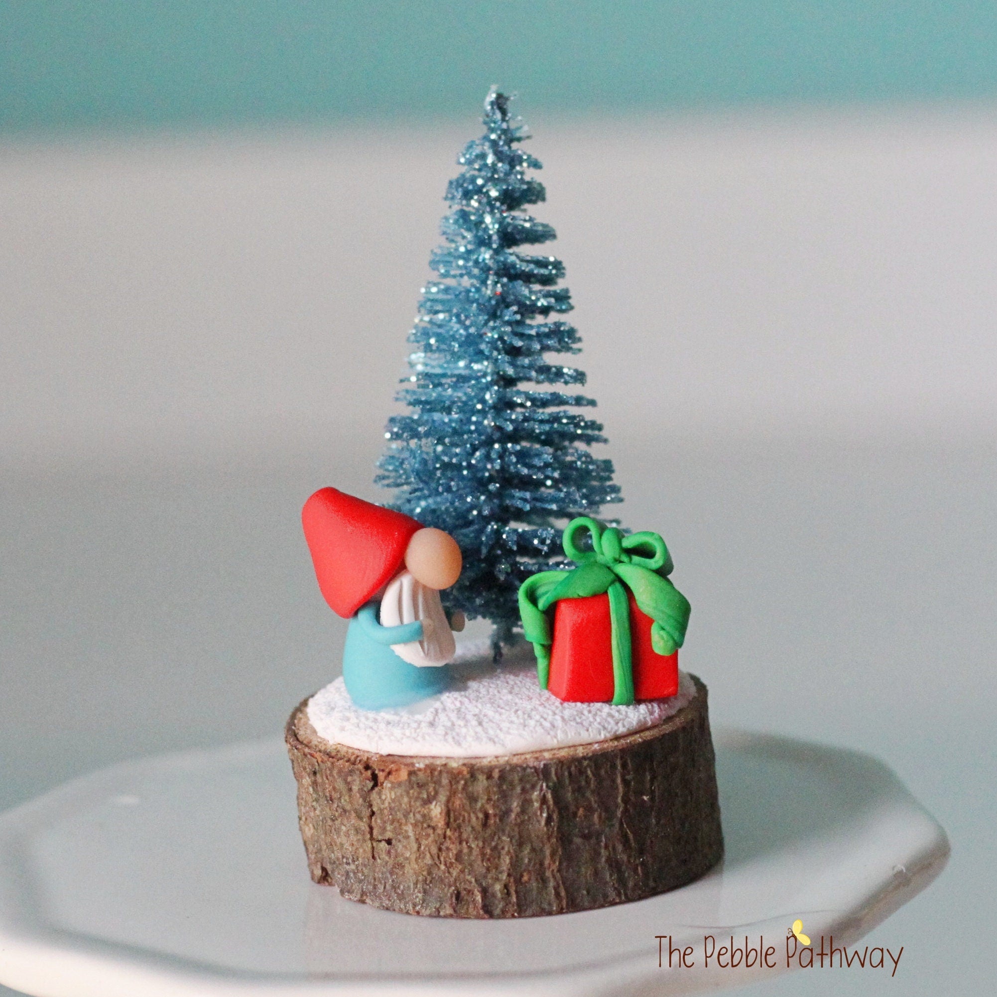Micro mini gnome with tiny present and blue glitter Christmas tree on wood slice - ThePebblePathway
