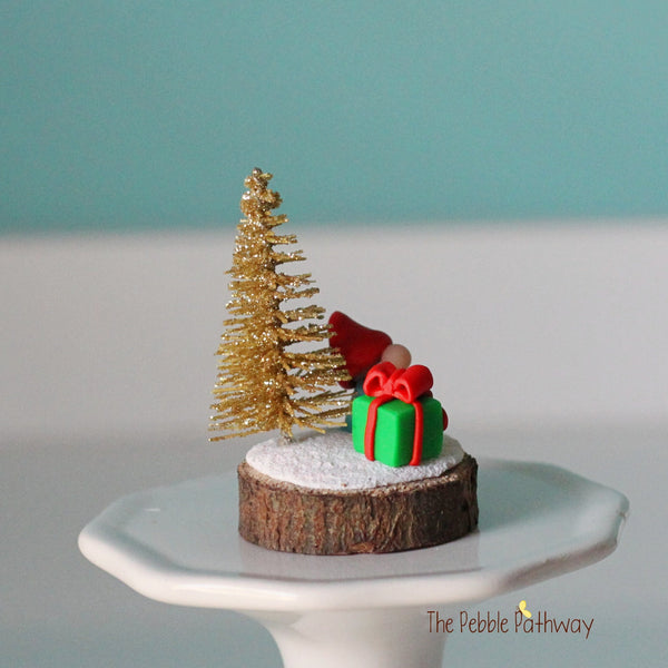 Micro mini gnome with tiny present and gold glitter Christmas tree on wood slice - ThePebblePathway
